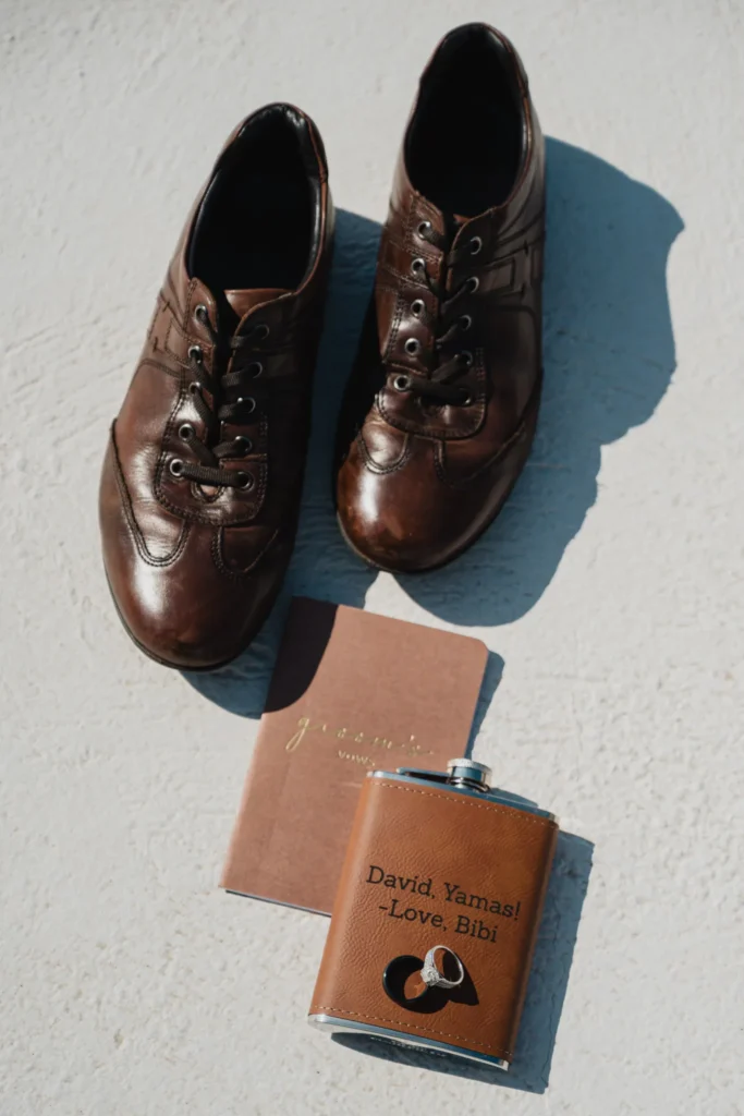 Angela & David wedding aboard a traditional Greek boat, Santorini — the groom’s shoes and an engraved hip flask
