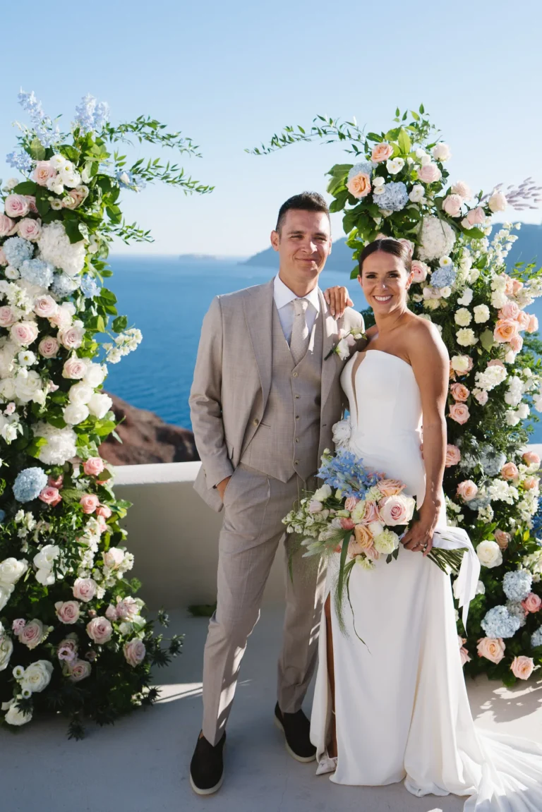 Elisa & Fabio wedding at Love Cave Venue, Santorini — the newlyweds between the floral pillars