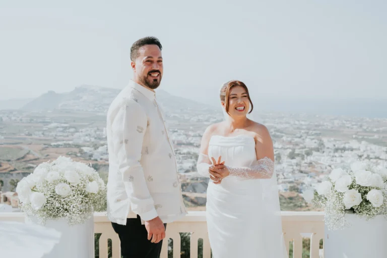 Hazel & Soltan wedding at Madame Sousou, Santorini — the bride and groom at the railing with the island behind them