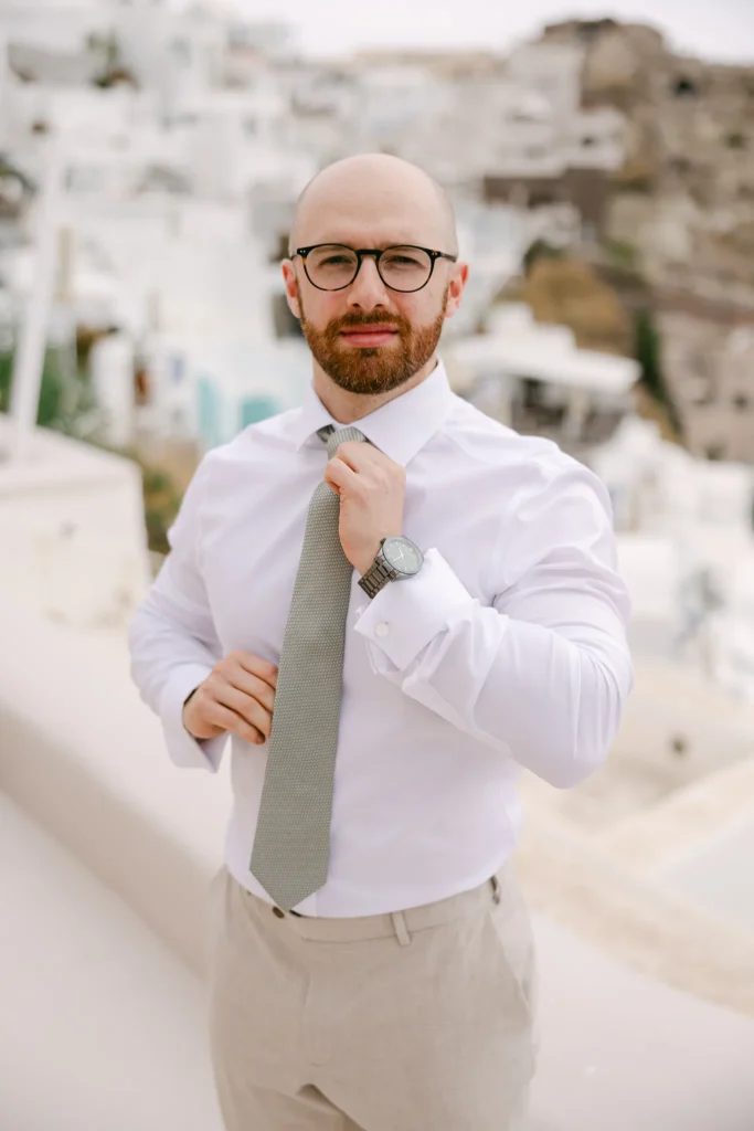 Loren & Matt wedding at Love Cave Venue, Santorini — the groom fastening his tie above Oia