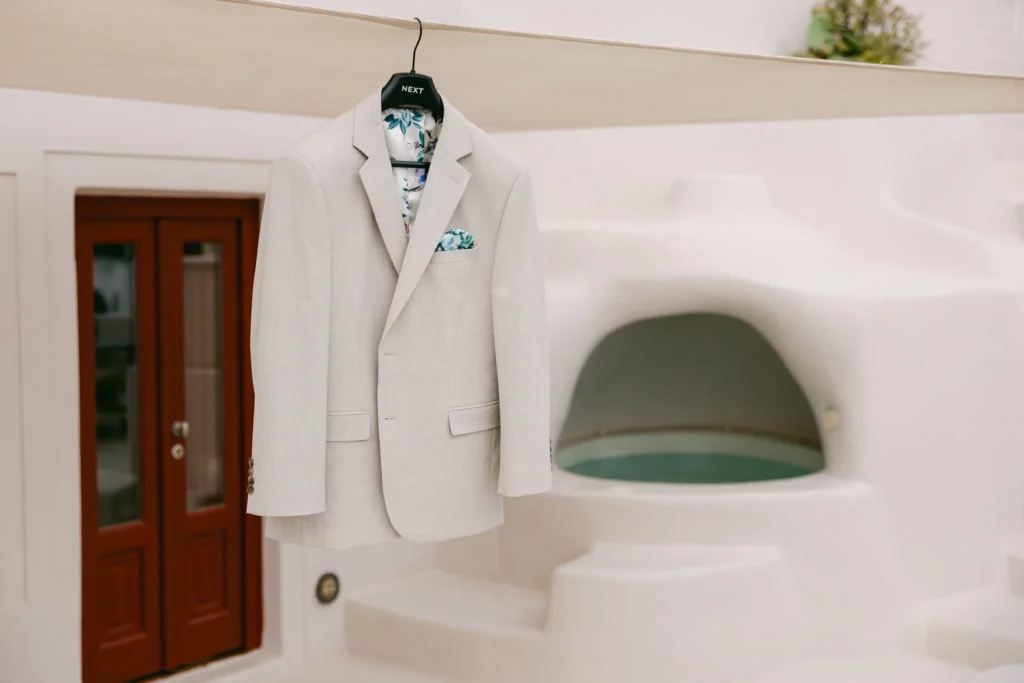 Loren & Matt wedding at Love Cave Venue, Santorini — the groom’s jacket hanging by a red door